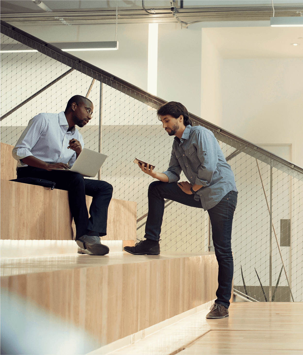 photo of two coworkers having a conversation on bleachers inside of an office presentation room.